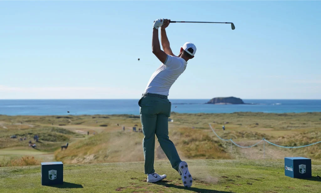 Golfer teeing off on a scenic course by the sea, showcasing stunning views and a calm atmosphere.